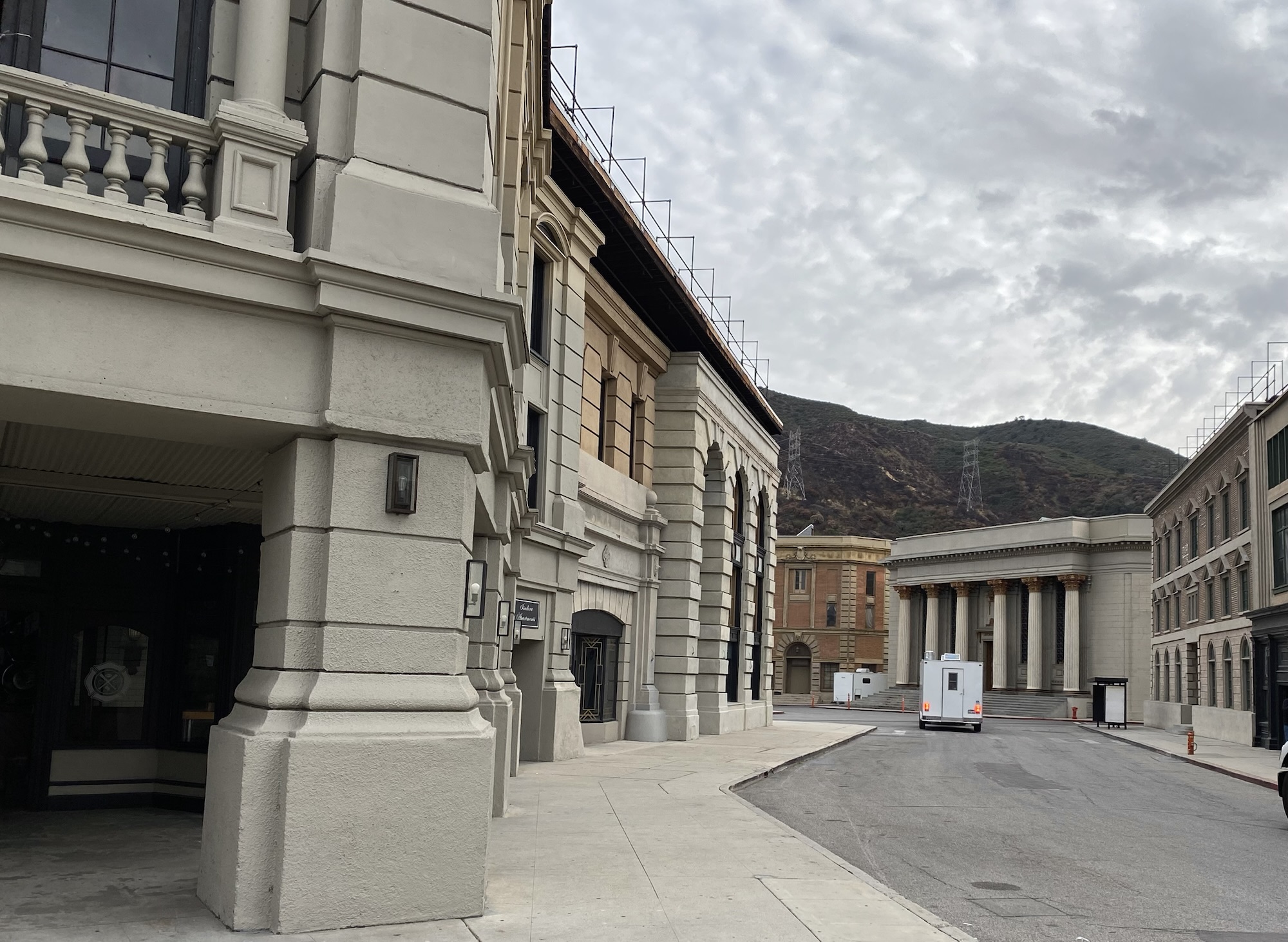 Quiet studio backlot street photographed at a major Hollywood studio, framed by soundstage buildings and mountains in the distance.